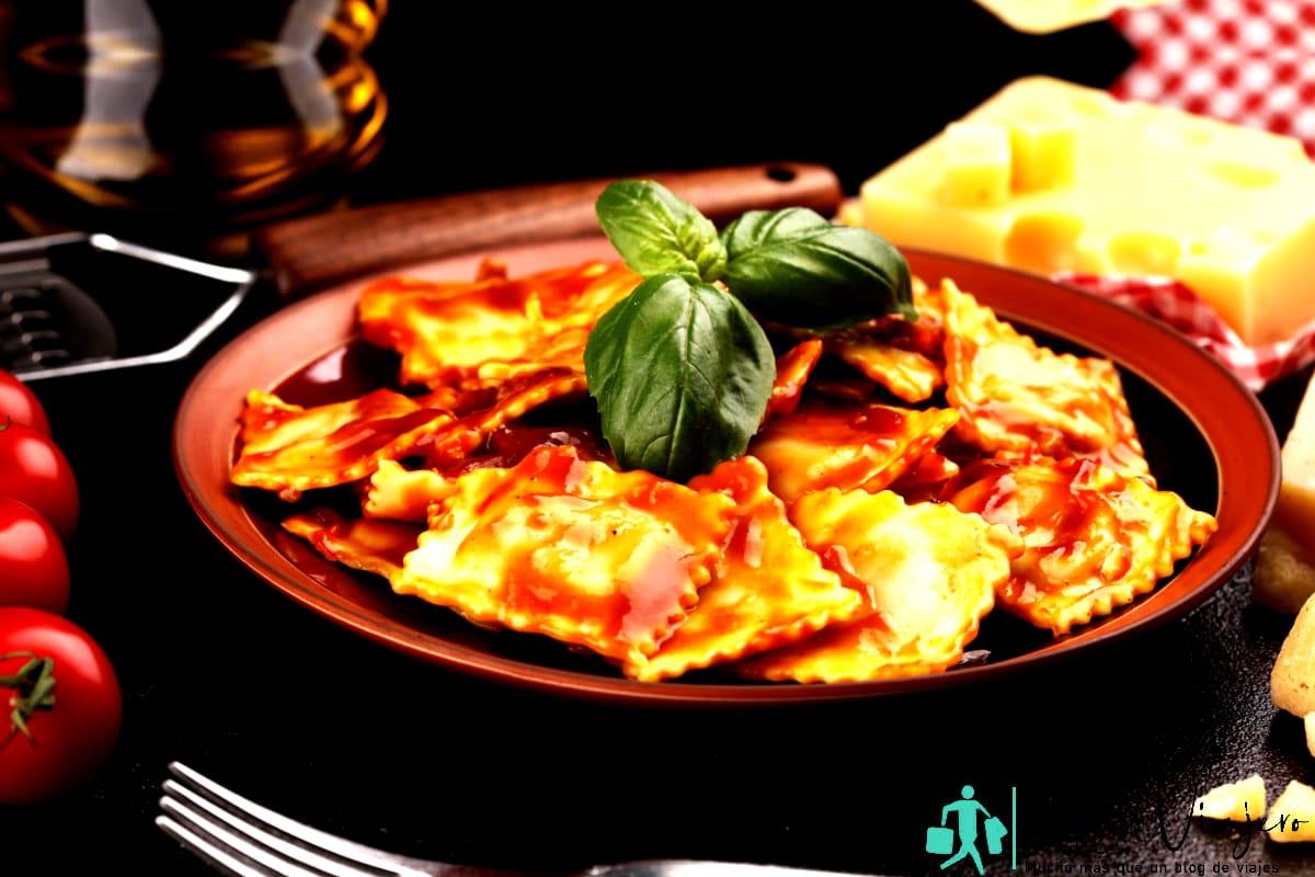 Ravioli con salsa de tomate aderezado con queso parmesano y albahaca sobre mesa